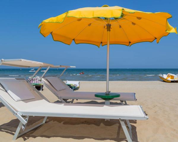 Strand mit Liegen, gelbem Sonnenschirm und Tretbooten im Hintergrund.
