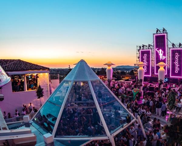Fête au coucher du soleil dans un club en plein air avec des lumières violettes.